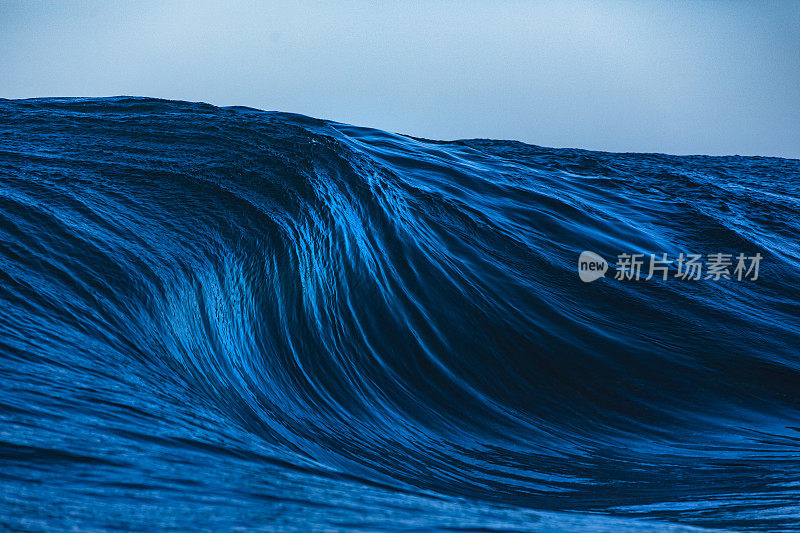 在晴朗晴朗的天气里，一个巨大的蓝色海浪在礁石上形成