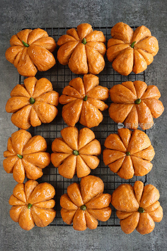图片上是一排排刚烤好的自制万圣节南瓜卷，上面有绿辣椒梗，面包上涂着杏酱，背景是斑驳的灰色，高架视图，聚焦于前景