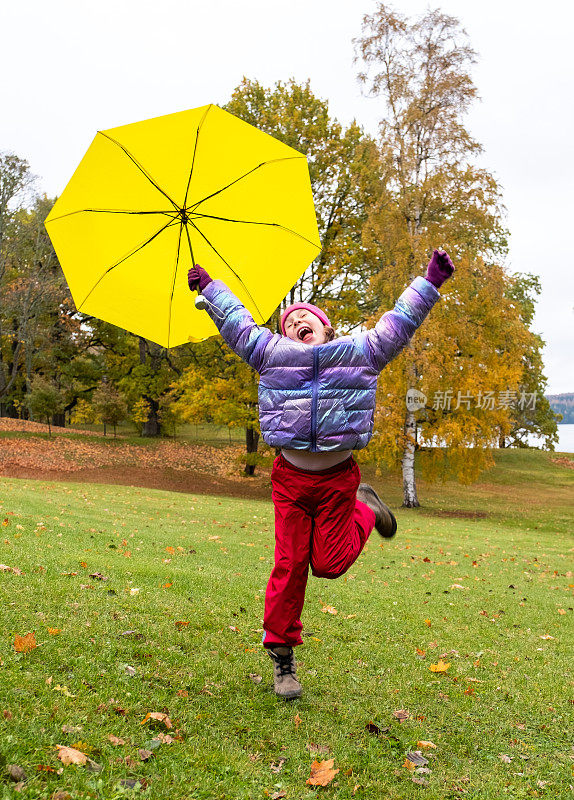 秋天，一个8岁的小女孩在公园里散步，手里拿着一把明黄色的伞。那孩子把胳膊伸到身体两侧，他很高兴。