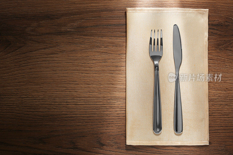 木桌上闪闪发亮的刀叉和餐巾，俯视图。文本空间