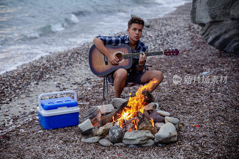 一个年轻人在沙滩上篝火旁弹吉他