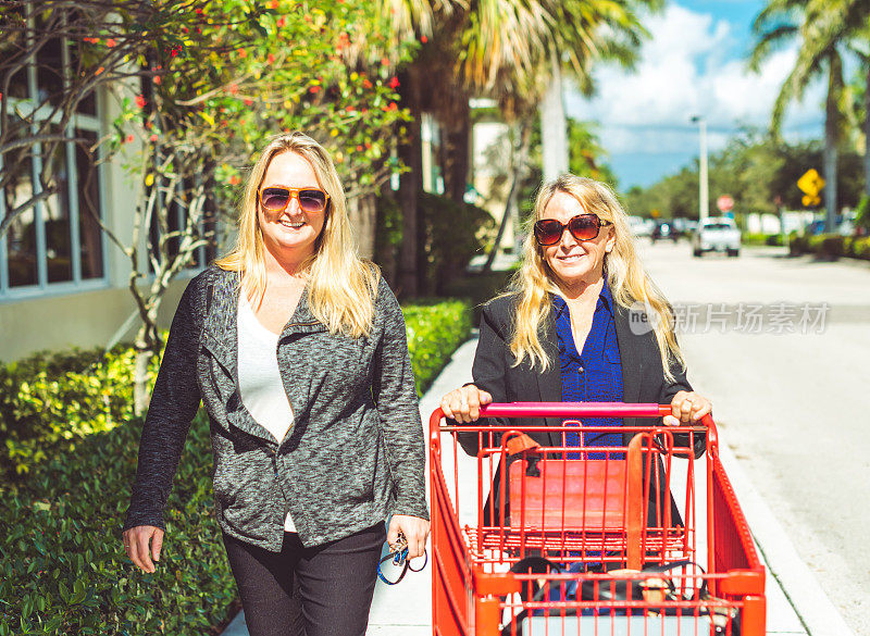 两个快乐的女人一起购物，在一家零售店外推着购物车