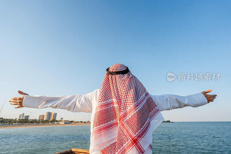 身穿头巾和头巾的年轻男子在科威特市的海滩上欣赏风景