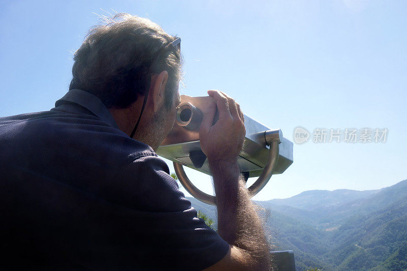 中年男子用投币操作的双筒望远镜看风景