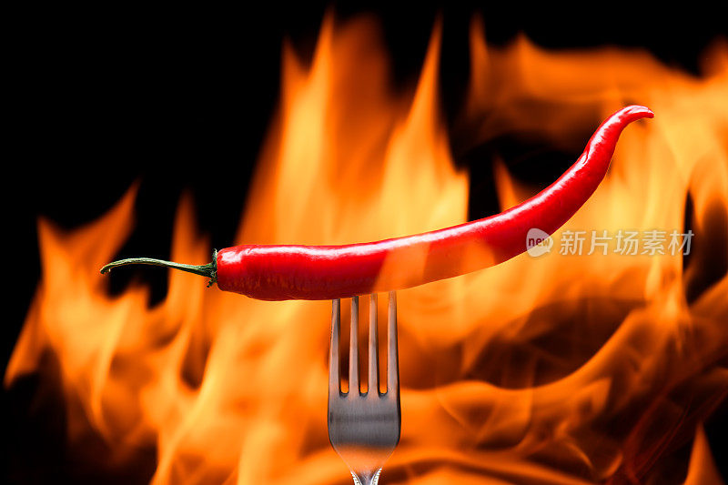红辣椒，用叉子戳着，背景是燃烧的火，火焰在黑色的背景上