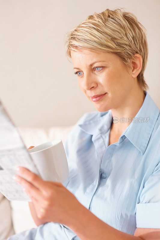 一位中年妇女，一边喝咖啡，一边看报纸