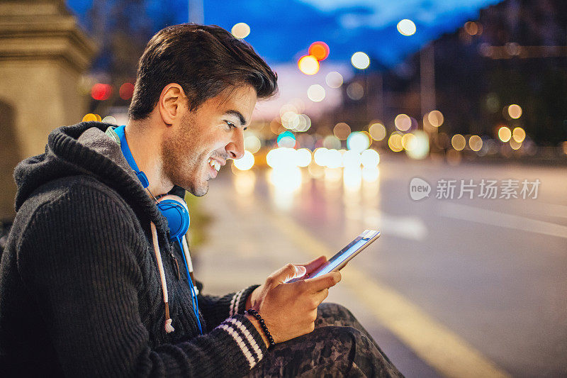 带着平板电脑和耳机的男人，在夜间的车流中外出