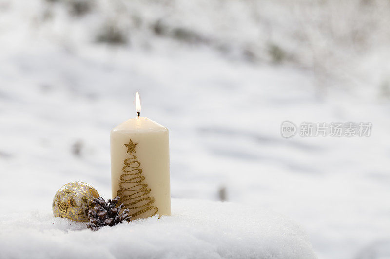 燃烧的蜡烛，圣诞的小装饰品和松果在雪中
