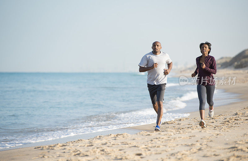 一对情侣在沙滩上跑步。