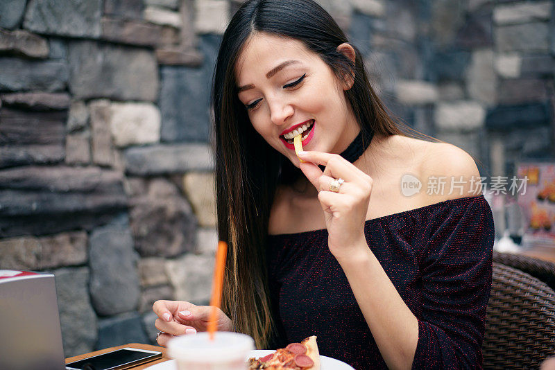 年轻漂亮的女人吃披萨和炸土豆