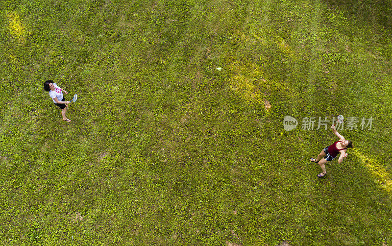 两个女人在草坪上打羽毛球。俯视图正上方，无人机拍摄