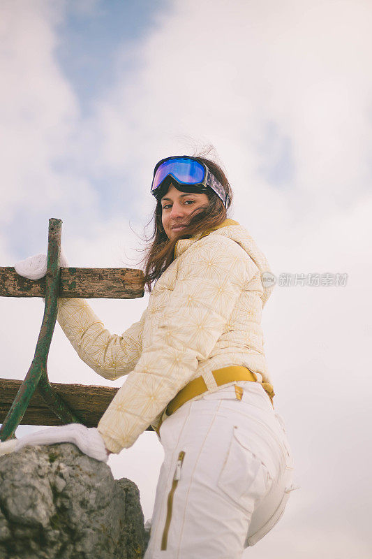 近景美丽的年轻女子在冬天的衣服站在一边，手拿木棍的背景雪山