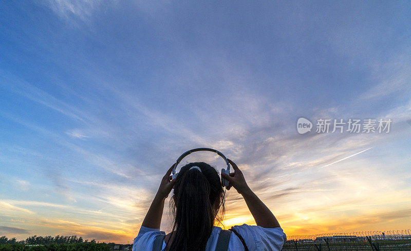 女孩戴着耳机，面对夕阳