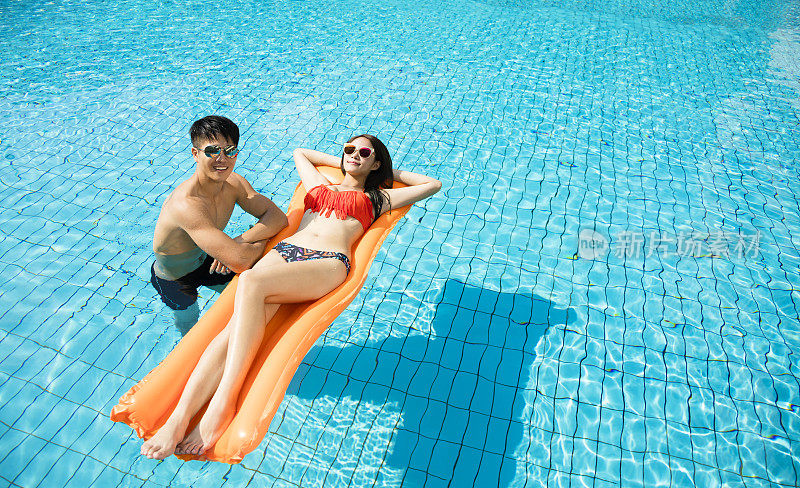 一对年轻夫妇在游泳池的充气木筏上放松