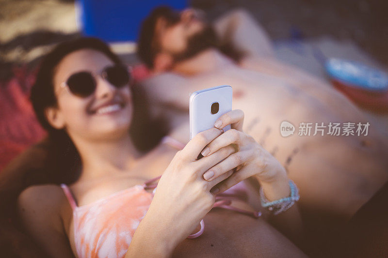 年轻女子和男友在沙滩上晒日光浴，发短信