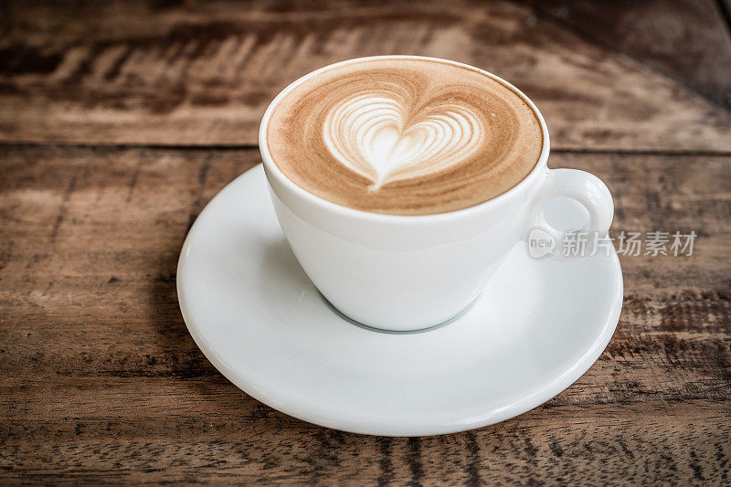 Drak色调滤镜，靠近白色咖啡杯与心形拉花艺术在咖啡馆的木桌上
