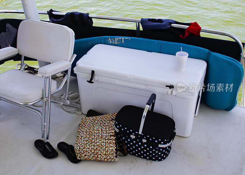 船的后部——椅子、冷却器、野餐篮、沙滩包和鞋子，通过船的后挡板漂浮在水里