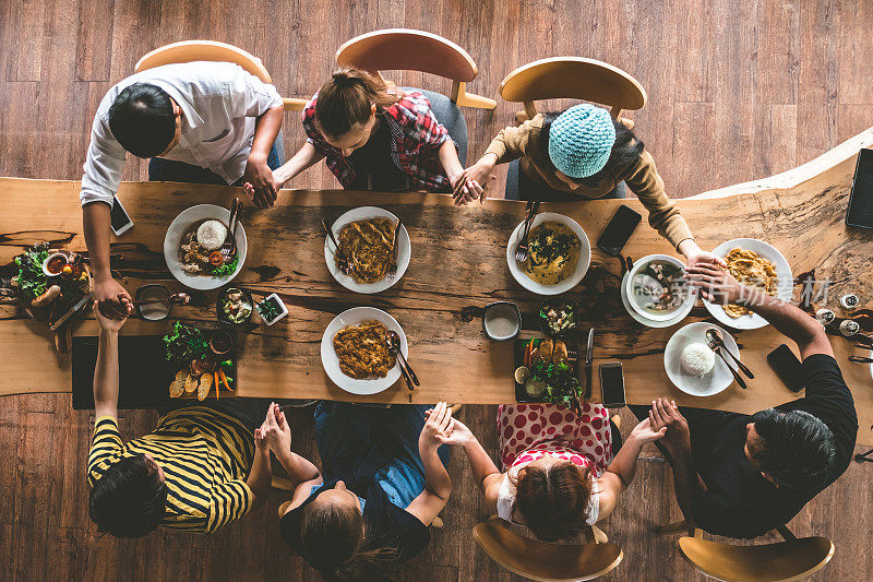一群朋友聚在一起祈祷，享用美味的食物和饮料，享受聚会和交流，俯瞰家人聚在一起吃晚餐。