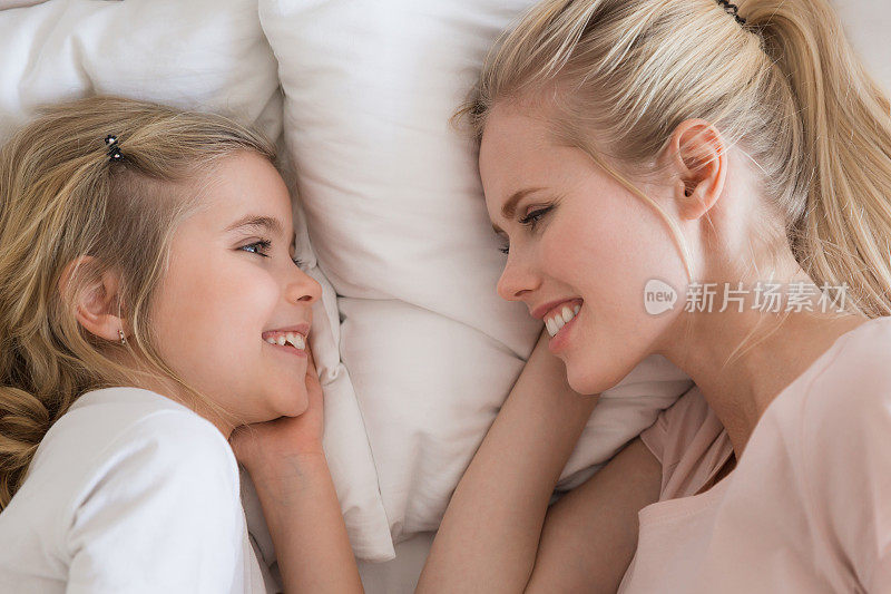 俯视图微笑的女儿和母亲躺在床上，看着对方