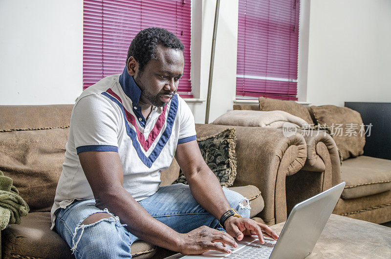 一个年轻的黑人坐在沙发上使用笔记本电脑