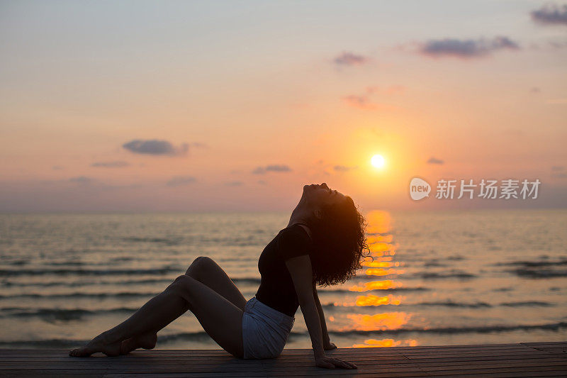 日落时分，年轻的亚洲女子坐在海边。