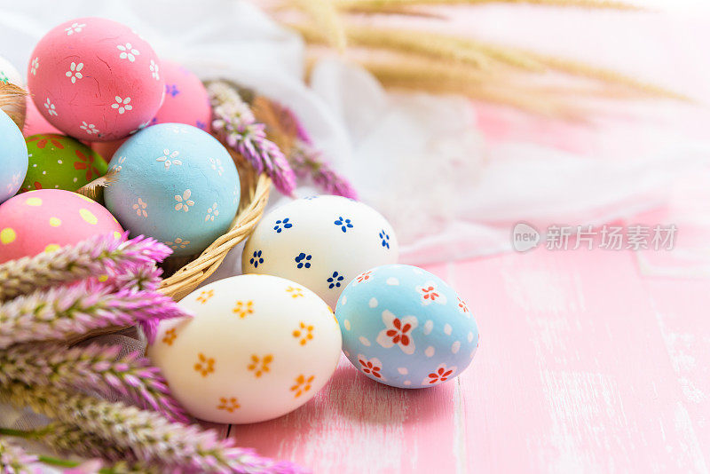 复活节快乐!色彩缤纷的复活节彩蛋在巢与纸星，花和羽毛在柔和的颜色明亮的粉红色和白色的木制背景。