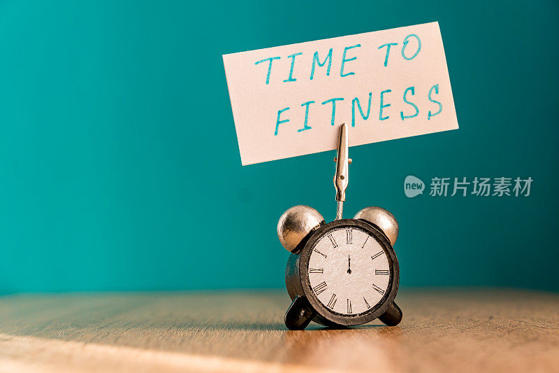 闹钟和写有“健身时间”的横幅放在木桌上。时间管理的概念。