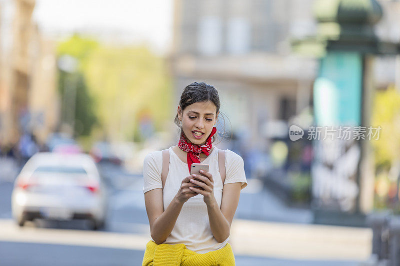 一名年轻女子正带着她的智能手机走在城市的路上