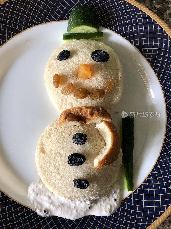 圣诞早餐雪人的食物艺术是用印度冬青年糕、黄瓜帽、椰子酸辣酱和葡萄干做成的雪人的眼睛和扣子