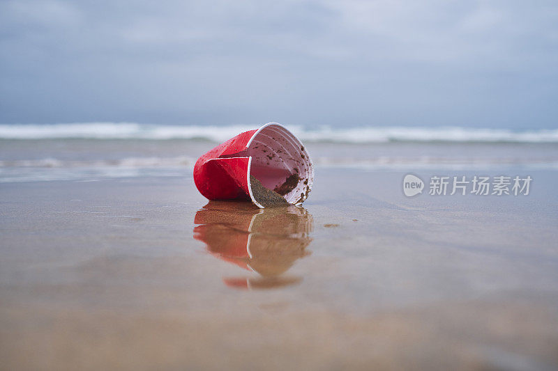 环境问题，被冲上岸的一次性红色塑料杯在海滩的海岸线。