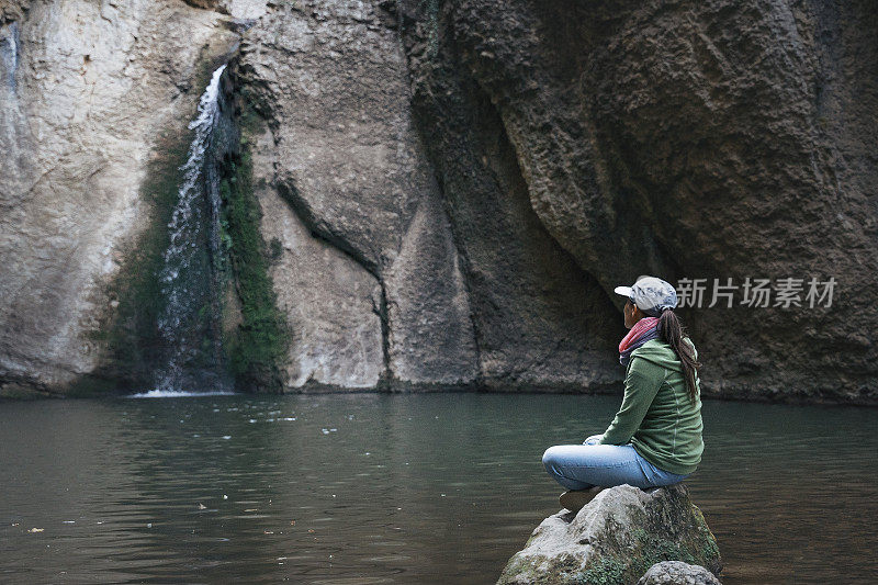 回归自然。独自旅行的人在瀑布附近冥想。一个快乐的年轻女性游客在自然。在阳光明媚的日子里在户外放松。