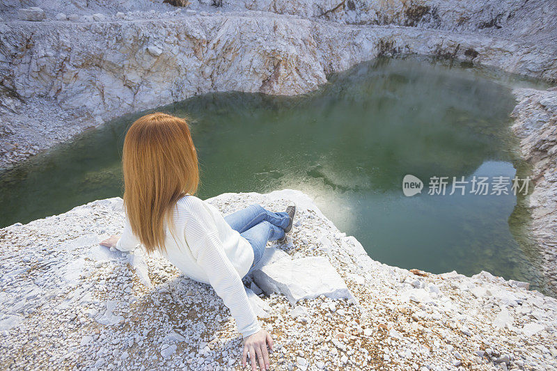 橙色头发的女游客坐在一个废弃的大理石采石场的悬崖边