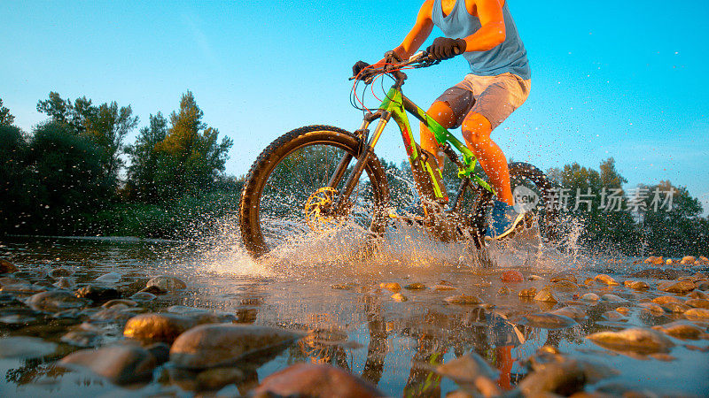 低角度:一名不知名的男性山地摩托车手将纯净的河水溅起。