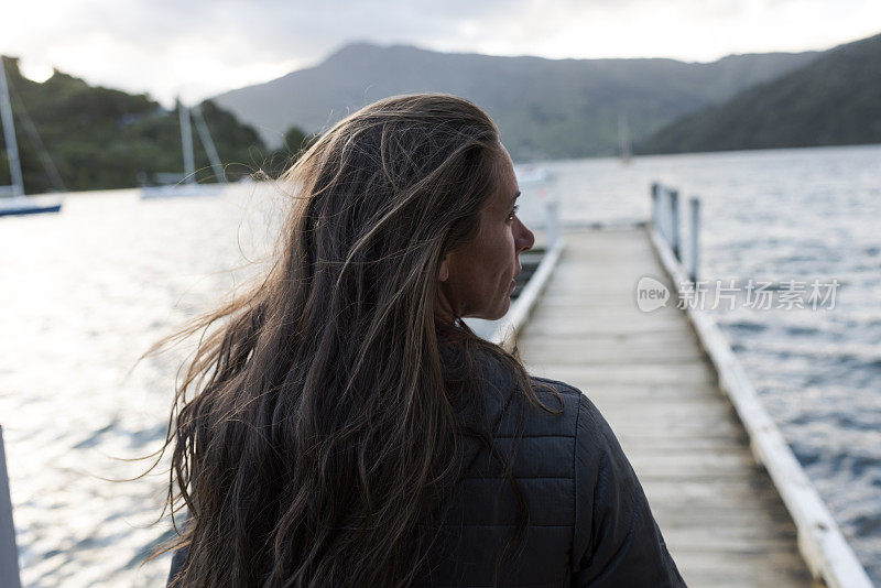 一个女人的后视图，站在码头上，看着湖