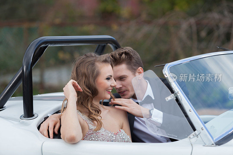 一对优雅的年轻夫妇坐在白色老爷车旁