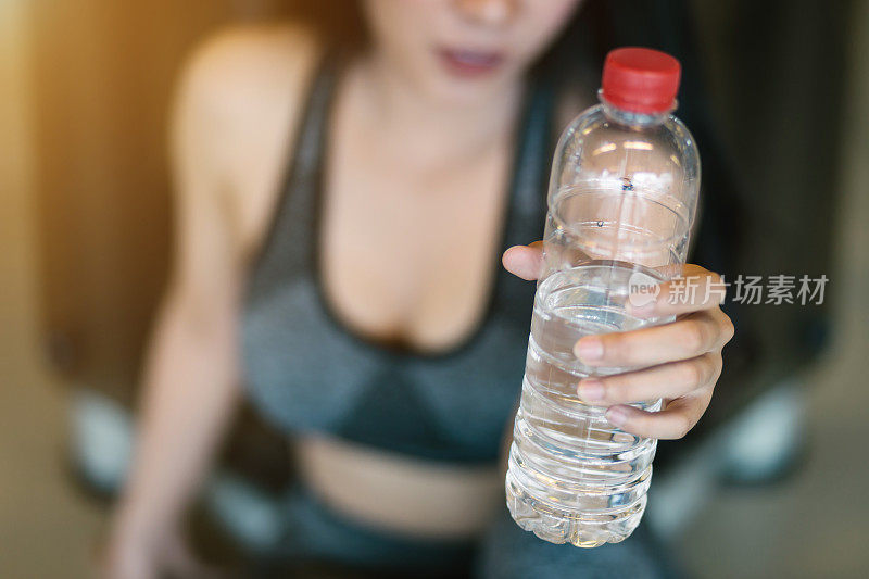 特写亚洲妇女进行锻炼训练，如何在体育健身室内和健身健身俱乐部与体育锻炼设备健身房背景的一瓶水。
