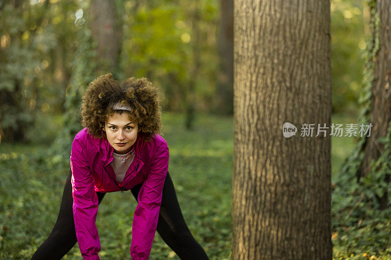 年轻的女性跑步者在晨跑前热身森林小径