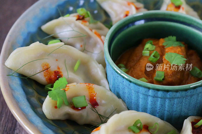 蒸饺(南亚饺子)，白面粉和水面团，充满鸡肉和杂烩蔬菜，淋上辣椒油，放在盘子里，周围是用橙色辣酱蘸酱的小模子，俯瞰美景