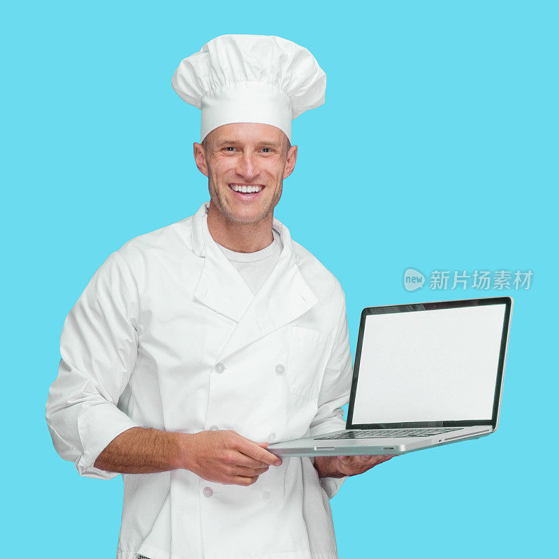 白种年轻男厨师站在蓝色背景下，穿着夹克，使用电脑