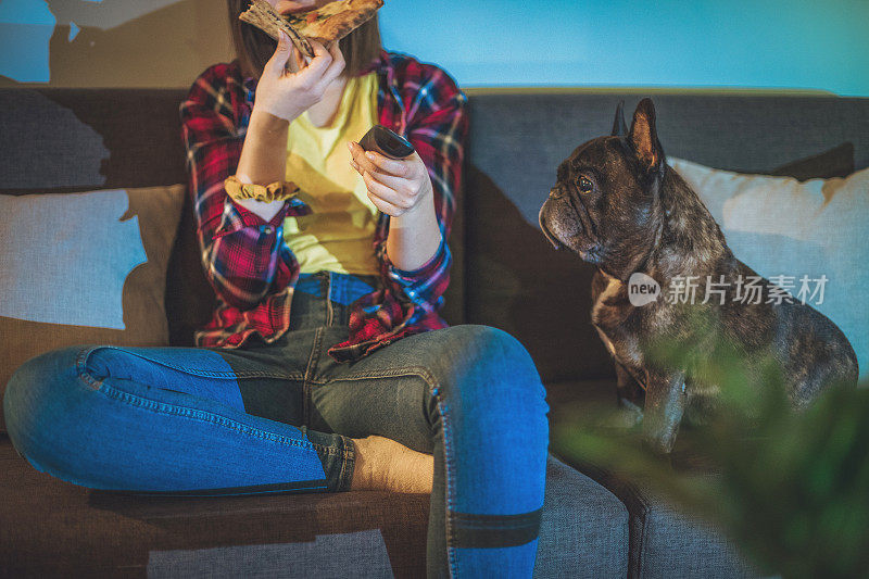 一个女人在沙发上吃披萨，和她的狗一起看电视