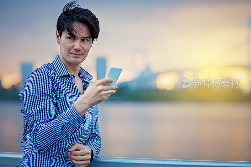 一名年轻的日本男子在东京城市和彩虹桥前发短信。