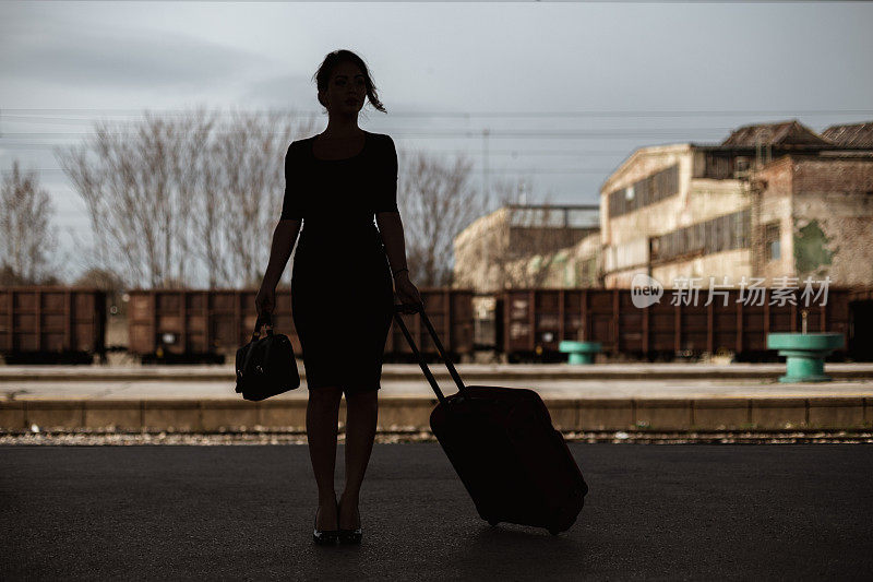 一个年轻女子在火车站拖着一个手提箱