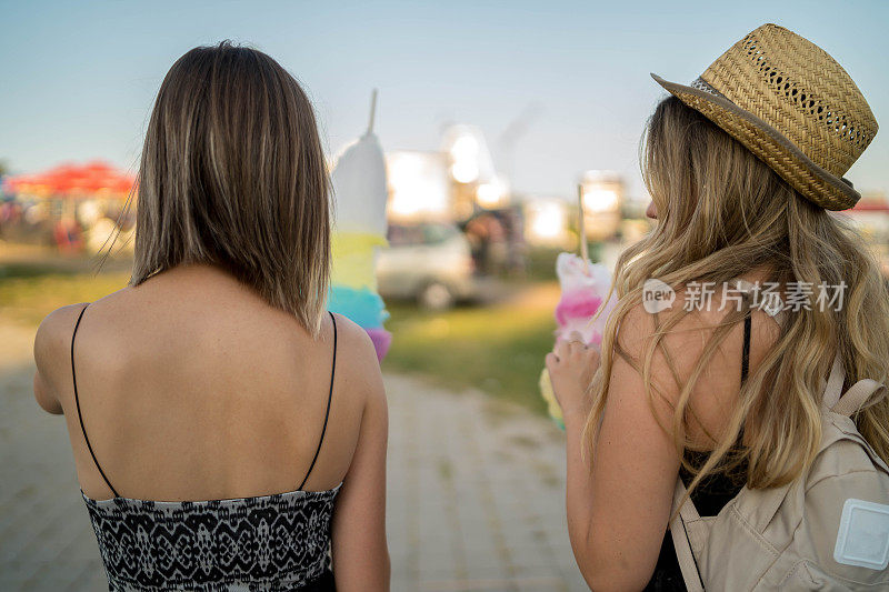 快乐的女性朋友在游乐园吃棉花糖的照片。两个年轻女人在游乐园玩了一天。