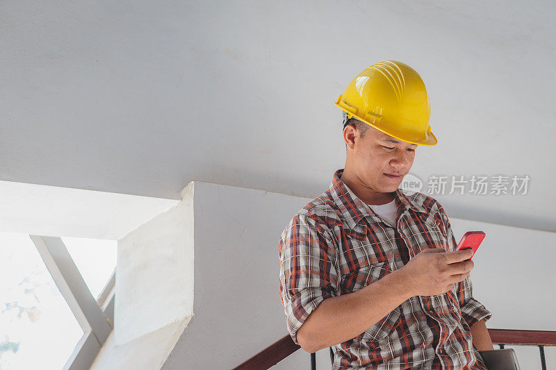 亚洲建筑工程师在安全帽中使用亚洲建筑工程师在安全帽中使用手机在施工现场，工程师在施工现场检查建筑施工项目