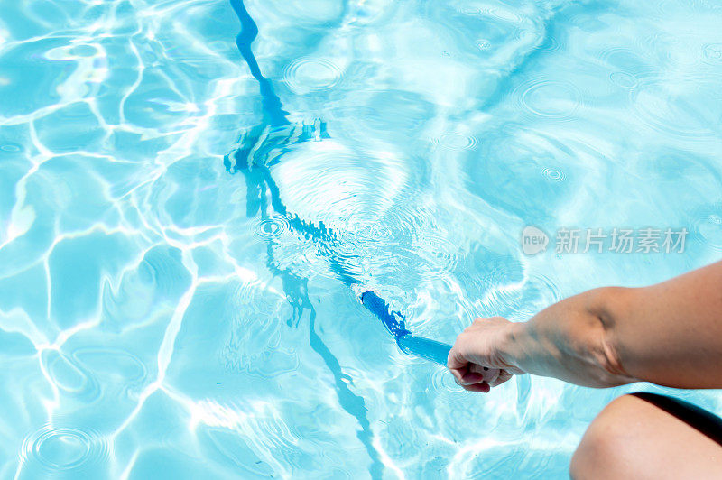 用真空吸尘器清洁游泳池的底部，里面有晶莹湛蓝的水和反射阳光