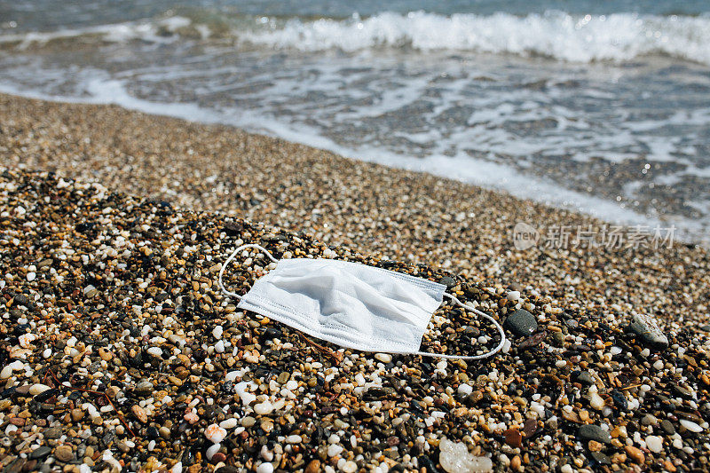 冠状病毒污染环境。海浪冲刷旧医用口罩废料库存照片