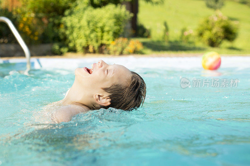 一个小男孩正在后院的游泳池里享受夏天的玩耍时光