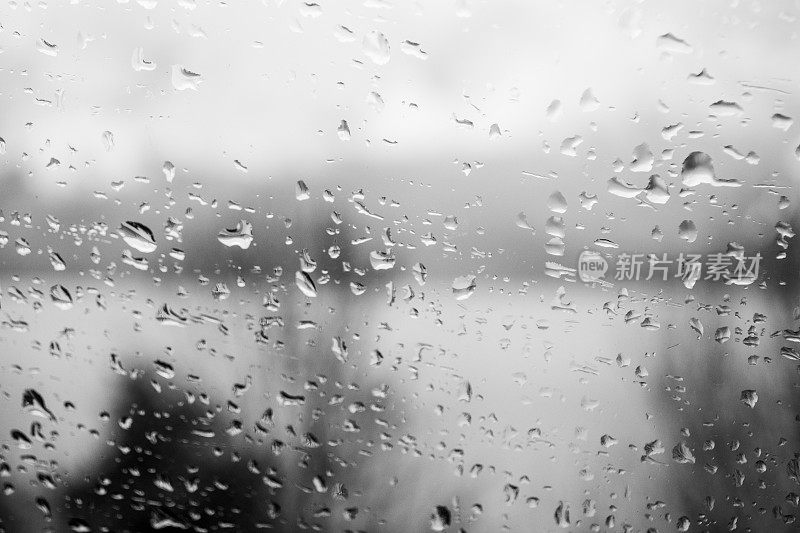 雨滴落在窗户上，描绘了白天灰色和下雨的天气。黑白灰度