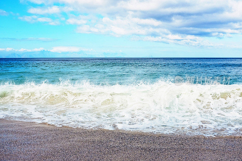 海浪拍打在田园诗般的海滩上，有地平线和部分多云的天空