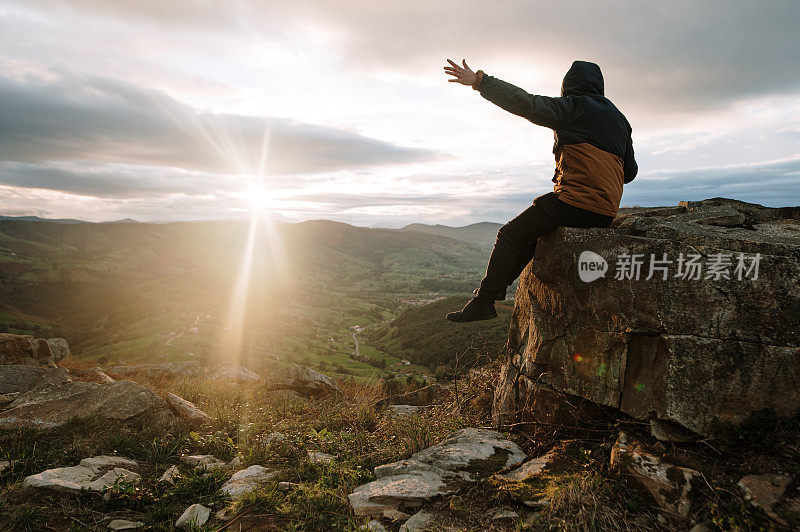 夕阳西下时，一个年轻人高举双臂坐在山顶上